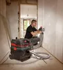 A man is using a drywall sander connected to a vacuum cleaner in a room under renovation. Podgląd zdjęcia produktu