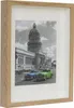 A framed picture of a building with two vintage cars in front. Náhled obrázku produktu