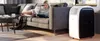 A woman is relaxing on a couch while using a tablet, with a portable air conditioner unit in the foreground. Produktbild-Vorschau
