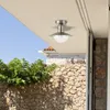 An outdoor ceiling light fixture mounted on a covered porch, with a stone wall and greenery in the background. Anteprima dell’immagine prodotto