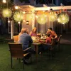 A group of people are enjoying a meal outdoors at night, with decorative lights hanging overhead. Voir les images du produit