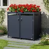 A dark gray double trash bin enclosure with a planter on top filled with red flowers, situated outdoors next to a brick wall and a grassy area with stepping stones. Produktbild-Vorschau