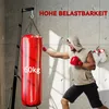 A man is punching a red punching bag, which is hanging from a stand. There are boxing gloves on the wall behind him. Produktbild-Vorschau