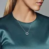 A woman wearing a teal satin dress and a silver necklace with a circular pendant. Anteprima dell’immagine prodotto
