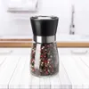 A pepper mill filled with peppercorns sits on a white wooden table in a kitchen setting. Produktbild-Vorschau