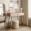 A pink console table with a wooden drawer knob and legs, a round beige stool, and several framed pictures on the wall. Produktbild-Vorschau
