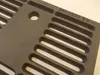 A close-up view of a dark gray cast iron grate with multiple oval-shaped openings and a circular hole. Anteprima dell’immagine prodotto