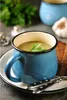 A close-up of a blue mug filled with soup, garnished with a parsley leaf, served on a plate with a slice of bread and cutlery. Produktbild-Vorschau