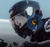 A person wearing a motorcycle helmet with a communication device attached. Náhled obrázku produktu