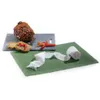 A piece of meat, bread, and chili peppers are arranged on a slate cutting board, with a roll of white netting on a green mat in the foreground. Podgląd zdjęcia produktu