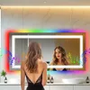 A modern bathroom with a large LED mirror, featuring colorful lighting and musical notes. Two women are visible, one in the foreground and one reflected in the mirror. Produktbild-Vorschau