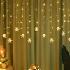 A string of snowflake-shaped LED lights hanging against a green curtain. Produktbild-Vorschau