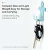 A light blue hook shaped like a person is attached to a white wall, holding a set of keys. Text describes the product's features. Produktbild-Vorschau
