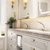 A luxurious bathroom vanity with two sinks and modern faucets, illuminated by wall sconces and under-cabinet lighting. Produktbild-Vorschau