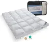 A white down comforter is laid out on a white surface, with a black carrying bag in the background. The comforter is quilted in a grid pattern. Several tags are attached to the comforter. Produktbild-Vorschau