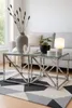 A living room scene with two glass-top coffee tables in the foreground, a sofa in the background, and a rug on the floor. Produktbild-Vorschau
