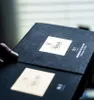 A close-up shot of an open dark gray box, revealing two cream-colored labels with branding and product information. Anteprima dell’immagine prodotto