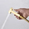 A hand holding a gold bidet sprayer with water spraying from it. Produktbild-Vorschau