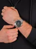 A person wearing a black hoodie and a silver watch on their wrist. Voir les images du produit