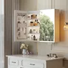 A white vanity cabinet with a mirrored door is open, revealing shelves stocked with toiletries and cosmetics. The cabinet is mounted above a white vanity table with drawers. Náhled obrázku produktu