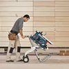 A man is moving a table saw on a stand with wheels. Voir les images du produit