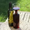 Two wine bottles and a wine glass filled with red wine are placed on a wooden table outdoors. Náhľad obrázku produktu