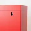 A close-up view of the corner of a red metal cabinet with a keyhole-shaped hanging slot. Voir les images du produit