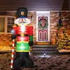 An inflatable nutcracker soldier decoration is placed on a porch for Christmas, with a wreath on the door and a decorated Christmas tree nearby. Produktbild-Vorschau