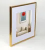 A gold picture frame with a white mat and a picture of a red flower inside. Produktbild-Vorschau