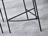 Close-up of the black metal legs and crossbars of a bar stool on a tiled floor. Produktbild-Vorschau