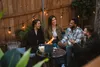 Four people are sitting around a small fire pit on a patio at dusk, enjoying each other's company. Produktbild-Vorschau
