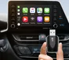 A hand holding a small black USB device in front of a car's infotainment system screen displaying Apple CarPlay. Produktbild-Vorschau