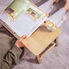 A person is lying on a bed with a wooden laptop table on their legs, reading a book and drinking coffee. Podgląd zdjęcia produktu