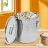 A stainless steel grain container filled with mixed grains, with its lid open and resting beside it. A small burlap sack of rice and a pile of rice are visible in the foreground. Náhled obrázku produktu