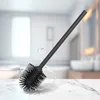 A black toilet brush with a silicone head and stainless steel handle is shown on a marble countertop with water splashing around it. The background is a blurred bathroom scene. Anteprima dell’immagine prodotto