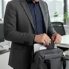 A person in a suit putting a laptop into a bag. Produktbild-Vorschau