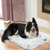 A black and white dog is lying on a fluffy dog bed in front of a fireplace. Produktbild-Vorschau