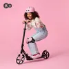 A young girl wearing a pink helmet and protective gear is riding a black scooter. Náhled obrázku produktu