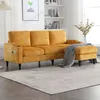 A yellow sectional sofa with an ottoman is set up in a living room with shelves and a lamp in the background. Náhled obrázku produktu