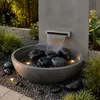 Schwarze Kieselsteine im Wasser einer Brunnen-Schale im Garten Produktbild-Vorschau