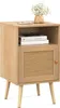 A light wood nightstand with a rattan door and a small vase of flowers on top. Produktbild-Vorschau