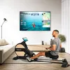 A man is using a rowing machine in a modern living room, with a large TV screen displaying a rowing simulation. Produktbild-Vorschau