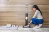 A woman is crouching next to a vacuum cleaner, with a pair of shoes on a mat nearby. Voir les images du produit