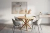 A round wooden dining table with four chairs on a rug, with a painting on the wall and a console table in the background. Voir les images du produit