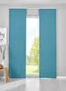 Two teal panel curtains are shown hanging in front of a window with a view of trees and grass outside. A small wooden stool with a decorative object is visible to the left.