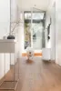 A white dog runs down a hallway towards the camera, with a large glass door and window in the background. Podgląd zdjęcia produktu