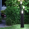 A modern outdoor lamp post with three illuminated columns stands in a garden at dusk. Produktbild-Vorschau