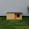 A wooden outdoor cat house with a circular entrance sits on green grass in front of a textured gray wall. Náhled obrázku produktu