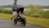 A man is jogging with a baby in a stroller next to a body of water. Náhled obrázku produktu