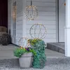Three illuminated spherical decorations are displayed on a porch with potted plants. Produktbild-Vorschau